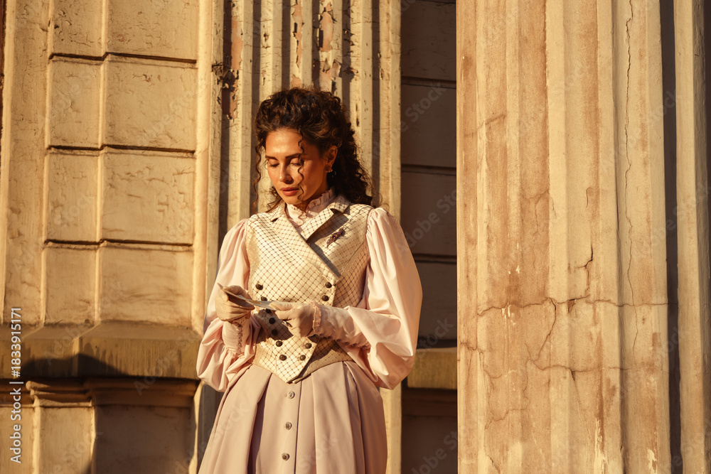 Fototapeta premium An elegant woman in a vintage dress stands by an old stone column