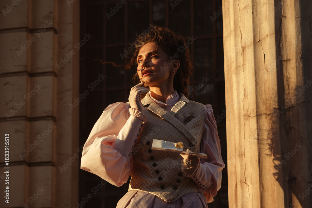 Fototapeta premium Portrait of a woman in vintage clothing, illuminated by warm sunlight, against a backdrop of ancient architecture.