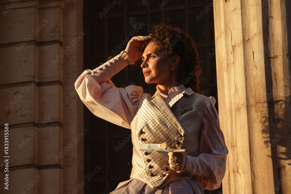 Obraz premium Portrait of a woman in vintage clothing, illuminated by warm sunlight, against a backdrop of ancient architecture.