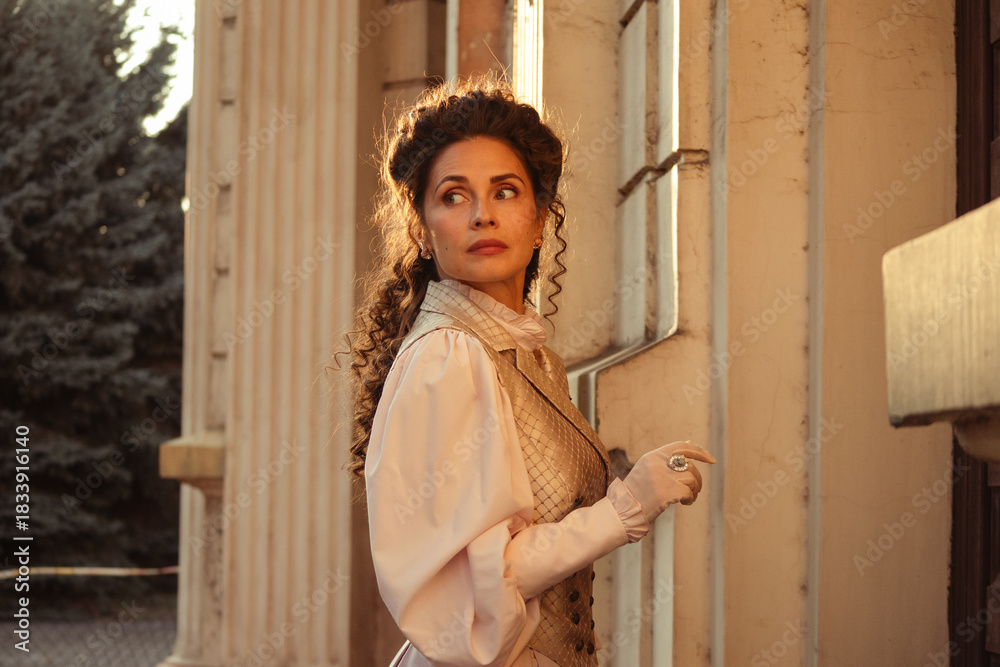 Fototapeta premium Portrait of a woman in vintage clothing, illuminated by warm sunlight, against a backdrop of ancient architecture.