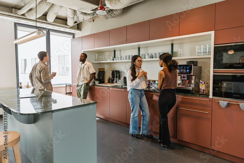 Two female workers are standing next to two male workers and they are talking while two of them are holding cups