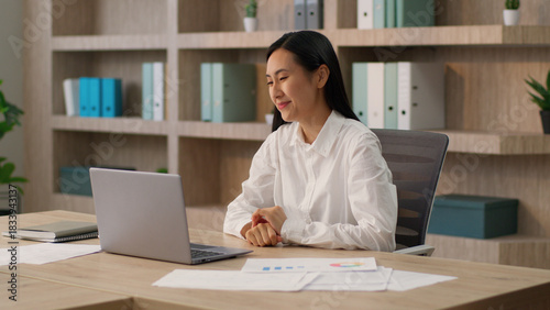 Happy laughing Asian Korean Chinese woman female worker Japanese girl boss businesswoman talking laptop pc waving hand hello gesture video call online conference computer business meeting in office