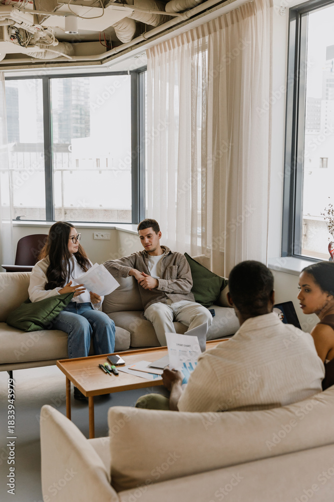 Fototapeta premium A group of four employees sit on sofas at a table and talk while two of them hold documents