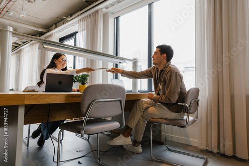 Male and female employees smiling and handing over documents while sitting at a table