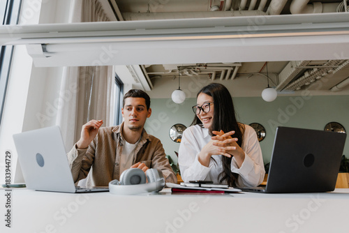 Male and female workers looking at laptop and sitting at table while she laughs