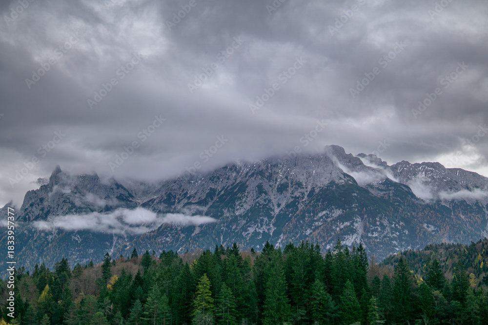 Obraz premium Snowy alpine mountains with forest and low clouds in misty autumn weather