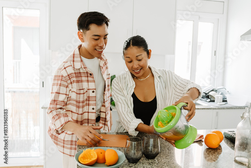 Принти на полотні Woman pouring juice from juicer into glasses while standing at table next to man