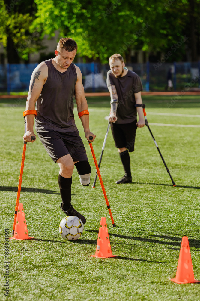 Obraz premium A man on crutches dribbles a ball between cones while a man on crutches looks on