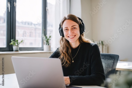 Portrait of a smiling woman wearing headphones during a webinar in a bright modern office