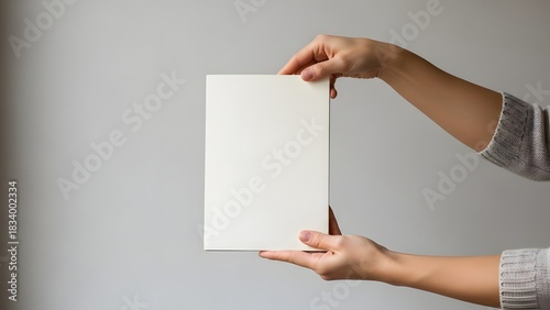 Hands holding a blank notebook against a neutral wall, soft natural light.