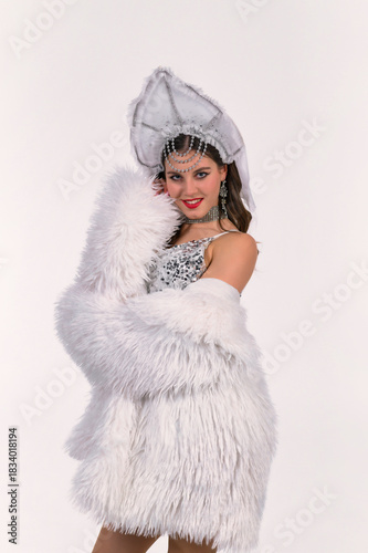 Model in a silver sequin dress, fluffy white coat and kokoshnik poses in a studio, showcasing a bright stage-inspired look with traditional accents and sparkling details