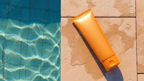 Orange sunscreen tube lying on a poolside tile next to clear blue swimming pool water on a bright sunny day