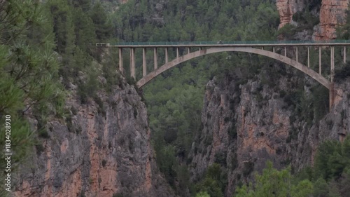 Motorcycle and Car Crossing Concrete Arch Bridge in Canyon