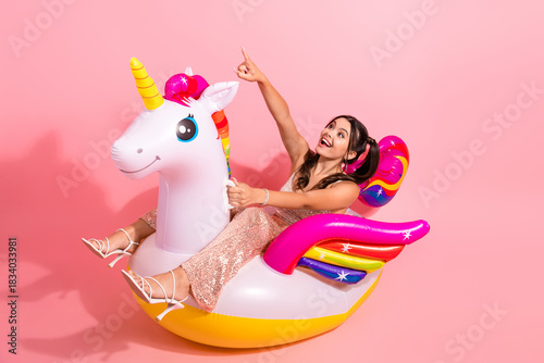 Young woman glittery pink dress rides colorful inflatable unicorn soft pink background festive lifestyle advertising campaigns holiday promotions
