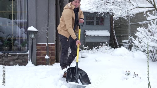 The first snow is falling. A heavy snowfall. A man is shoveling piles of snow from the yard.