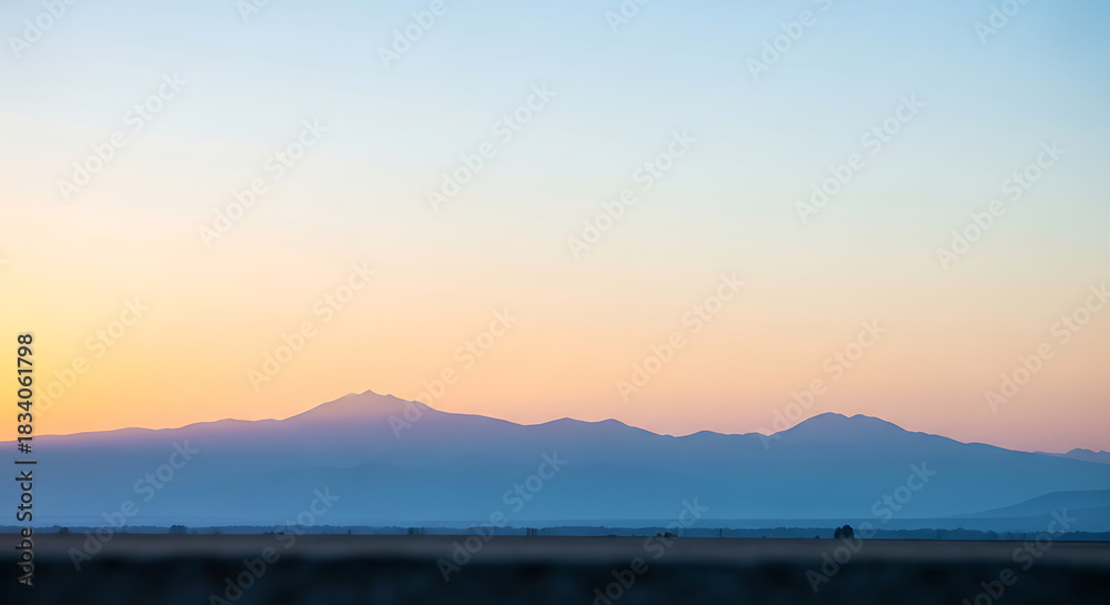 Fototapeta premium Serene Mountain Range Silhouette at Sunset with Soft Pastel Sky