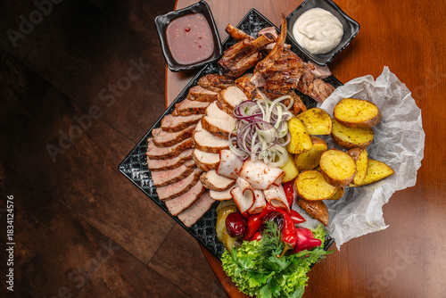 assortment of grilled and smoked meats served with roasted potatoes, fresh vegetables, sliced onions, herbs, and two types of sauces on a large platter. restaurant menu