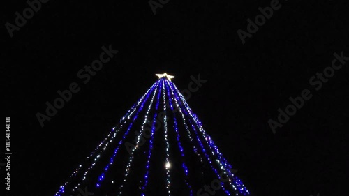 A twinkling Christmas tree against a dark sky background. Animation of Christmas tree lights glowing.