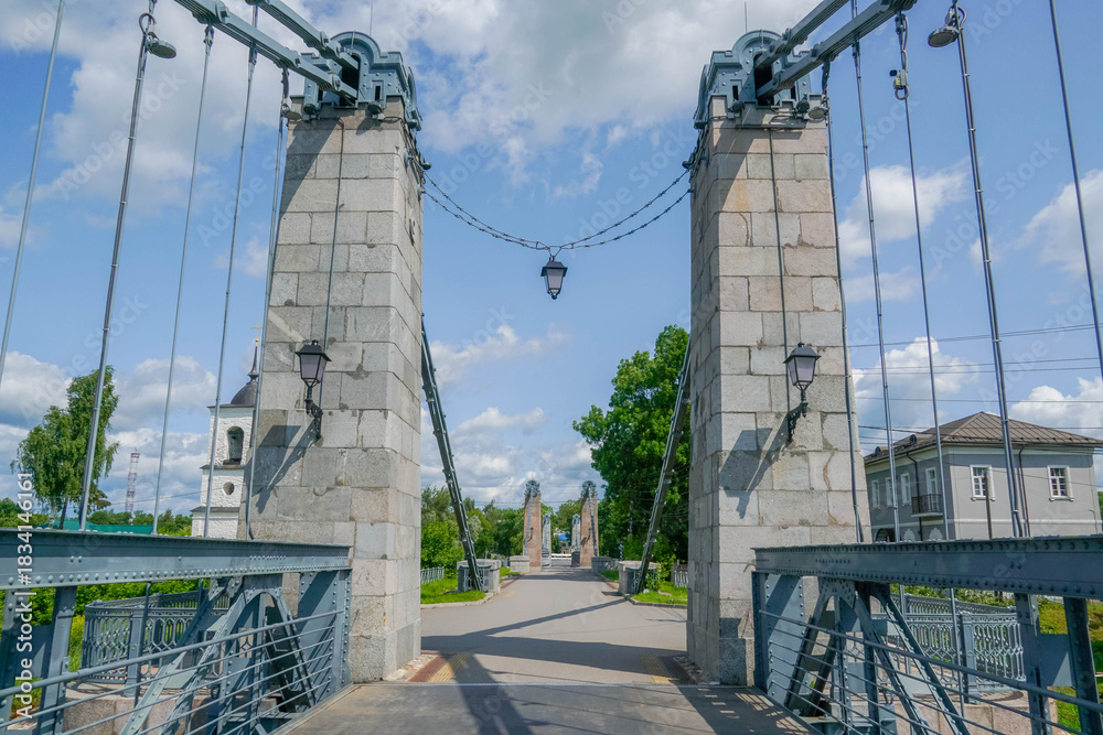 Fototapeta premium Massive stone pylons and steel cables of Ostrov’s historic suspension bridge over the Velikaya River in Pskov oblast, Russia. stock photo 