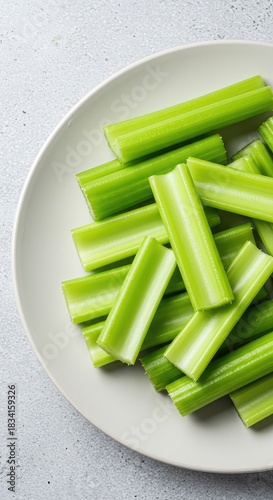 A simple white platter filled with freshly cut, bright green, crisp celery stalks, ready to be dipped and eaten as a healthy, vegetarian snack ,closeup ,raw ,fresh