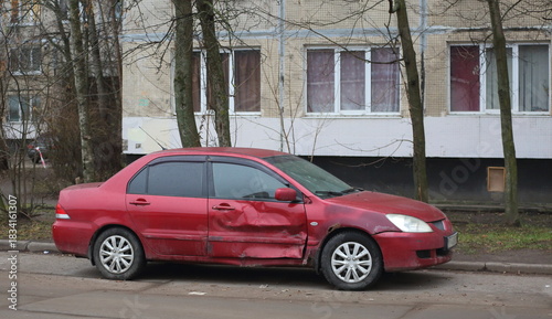 Fotografija A dented red car is parked near a residential building, Podvoyskogo Street, Sain
