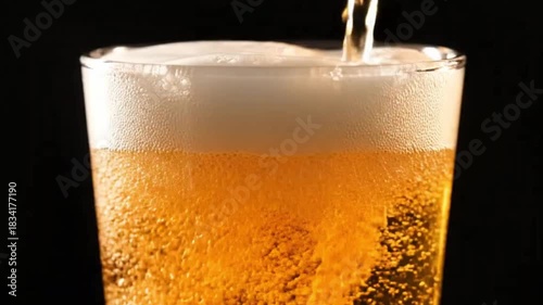 Wallpaper Mural A captivating close-up shot captures the dynamic action of a golden, effervescent liquid being poured into a clear glass, creating a rich, frothy head of white foam. The vibrant amber hue of the bever Torontodigital.ca