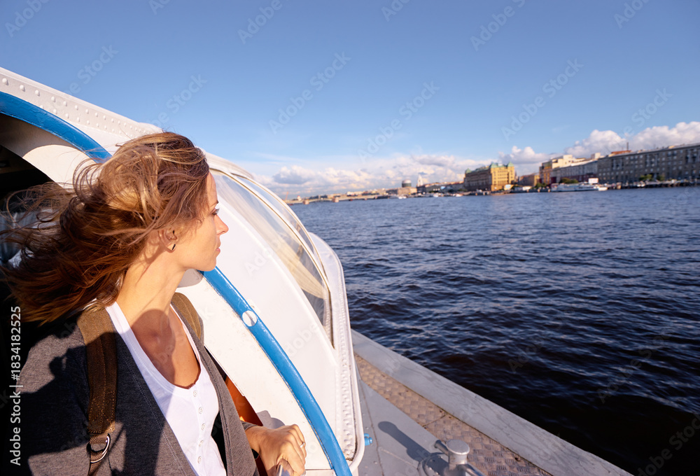 Fototapeta premium Young woman on a deck of a boat observs a cityscape coastline. Petersburg, Russia.