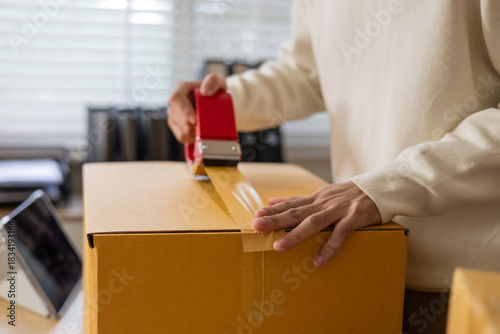 Warehouse shipping workflow showing young worker attaching label to parcel, preparing delivery orders, managing ecommerce packing process, supporting logistics operation in small business storehouse