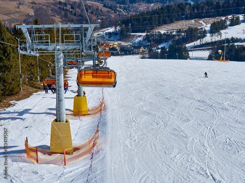 Orange Ski Chairlift Tower Over a Snowy Slope with Distant Skier