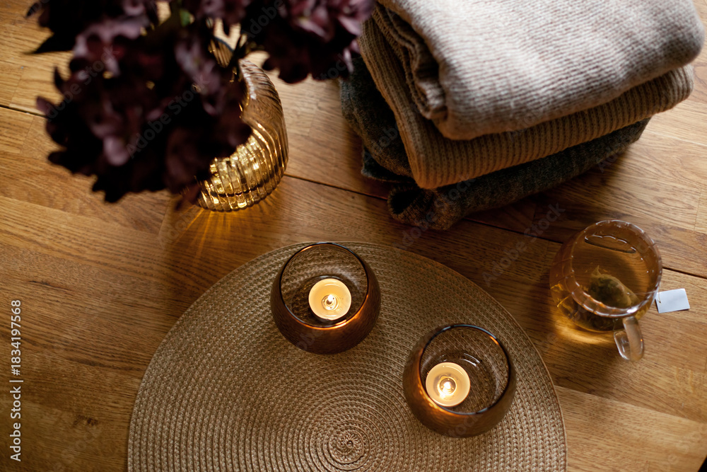 Naklejka premium Home interior decor in brown colors: glass vase with dried flowers, candles and cup of warm tea