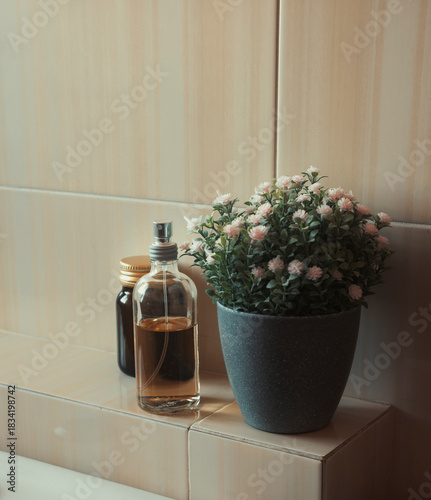 Elegant perfume bottle next to flowerpot with pink flowers decorating bathroom. Mockup design template.