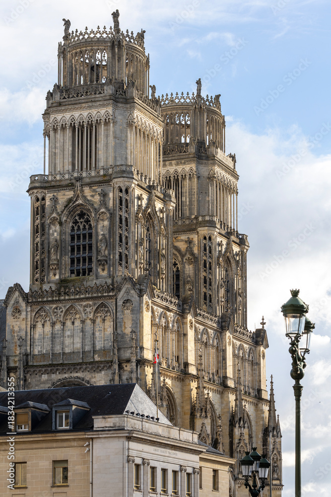 Fototapeta premium Gothic Orleans Cathedral towers rising behind Hotel de Ville building facade. Historic French architecture landmark in Loiret region with flag on roof against cloudy blue sky on a sunny day