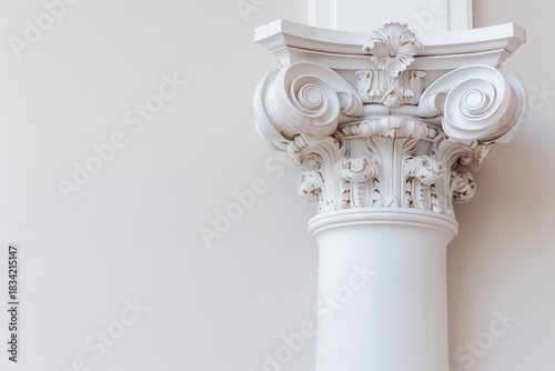 A classical column stands against a plain wall. The base of the column features intricate designs and ornamentation. The background is mostly empty, allowing the column to be the main focus
