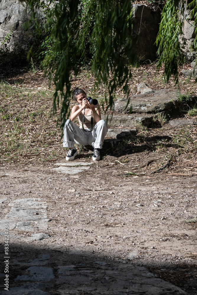 Fototapeta premium Girl taking a photograph in nature while sitting on the floor.