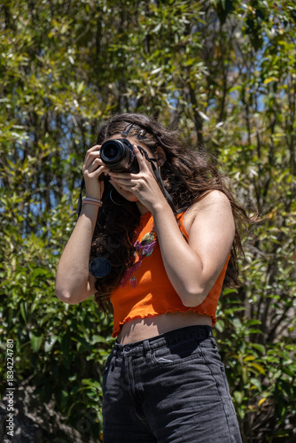 Young girl holding a camera and taking photographs in nature.