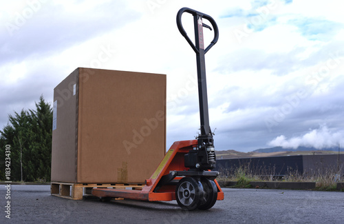 Pallet jack transporting large cardboard box outdoors on industrial pavement
