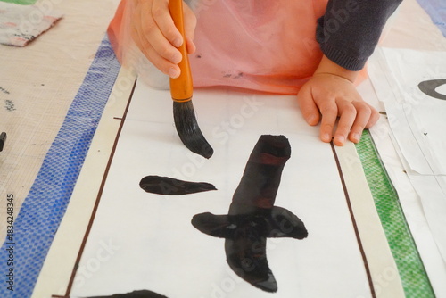 子どもが筆で太く力強い文字を描いている書道シーン。墨の濃淡や筆遣いの迫力が伝わる、習字練習のリアルな表現。学校宿題、教育教材、書道指導イメージにも活用できる素材。
