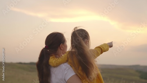 Obraz na plátně child with mother hugging at sunset, children shows mom by hand at sunset, childhood dream, happy family, love to travel together with family, kid and parent in nature sun, little daughter mom arms