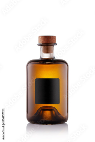 A clear glass bottle stands upright against a white background. The bottle is filled with amber liquid and has a wooden cap. A blank label occupies the front of the bottle.