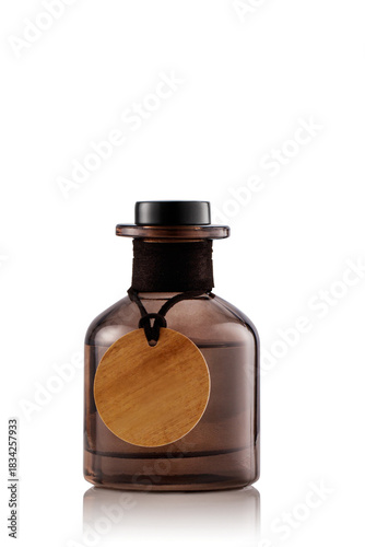 A brown glass bottle with a cork lid sits upright on a smooth white surface. The bottle has a round wooden tag attached to its neck. This setup gives a clean and uncluttered look.
