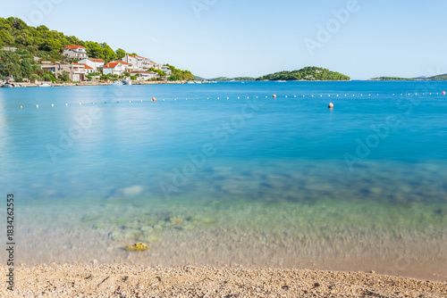 Fototapeta Naklejka Na Ścianę i Meble -  The seaside town of Tisno in Croatia is situated on the shores of a blue sea with many hills, the landscape on a sunny summer day, view from the beach.