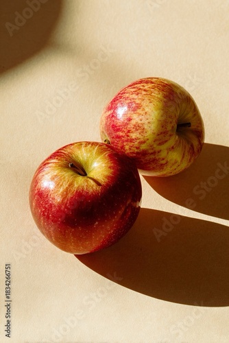 Due mele rosse su un tavolo, illuminate dal sole, evidenziando la loro lucentezza e freschezza.
