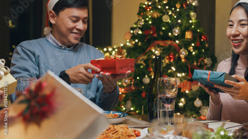 Group of Asia colleague friends gathering New year holidays party together. Group happy of friends laughing and sharing gifts on christmas dinner at home in evening, celebration and people concept.