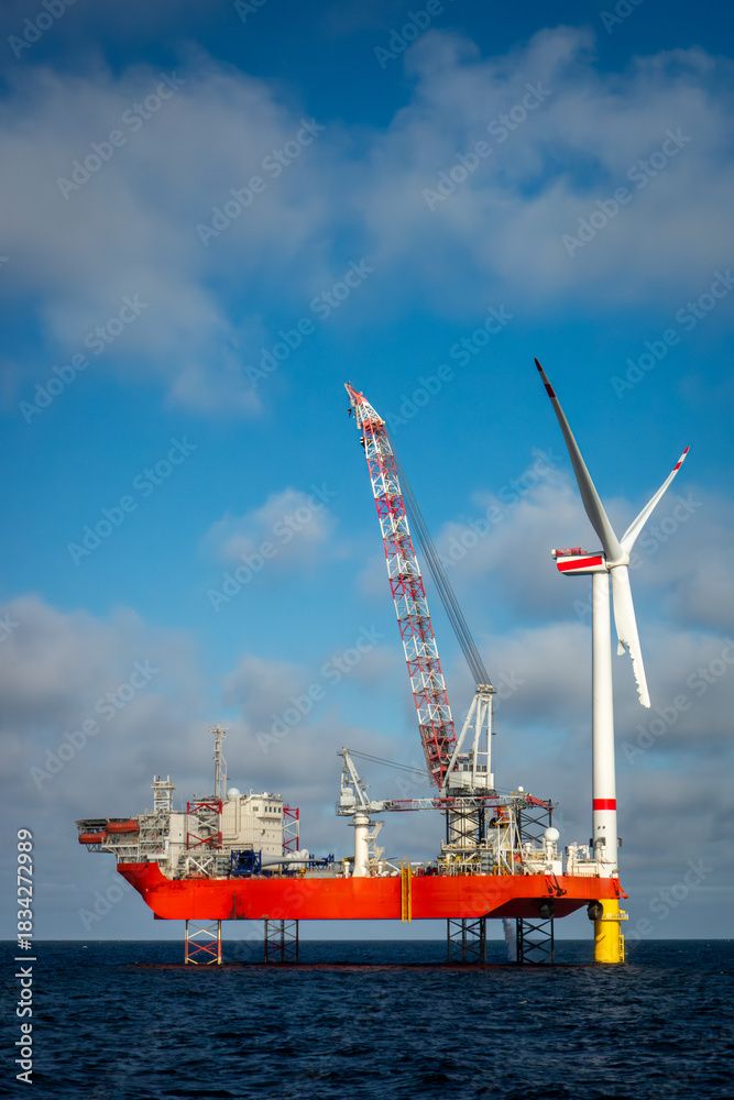 Fototapeta premium Offshore wind farm construction with a heavy-lift jack-up vessel installing a giant turbine. Renewable energy construction, offshore engineering, sustainable power infrastructure