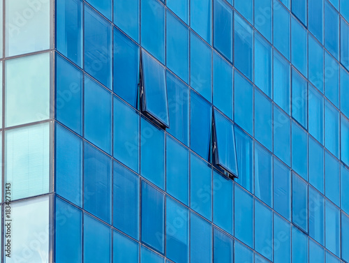 Modern glass office building facade with blue reflective windows and open ventilation panels. Contemporary architecture, urban design pattern, corporate exterior background
