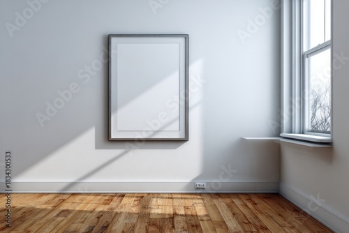 Empty picture frame hangs on pale wall beside window with natural light casting shadows across wooden floor