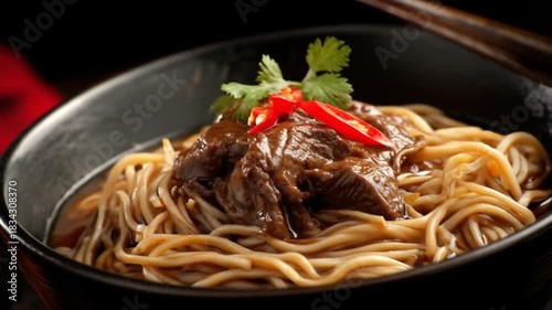 A dark bowl of flavorful beef noodles, highlighted by vibrant spices and garnishes.