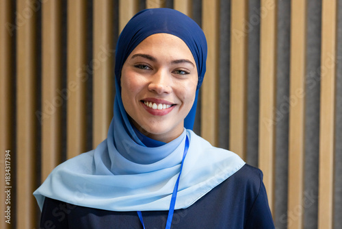 Female smiling and posing for portrait at conference lobby, wearing two-tone blue headscarf lanyard