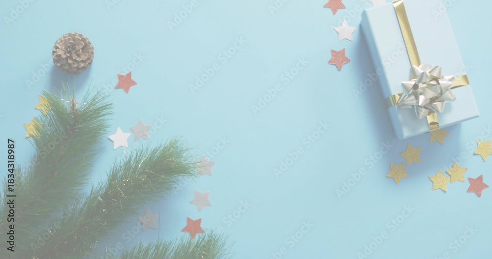Fototapeta premium Sitting light-blue-gift gold-ribbon silver-bow on pale-blue surface firsprig cone stars, copy space