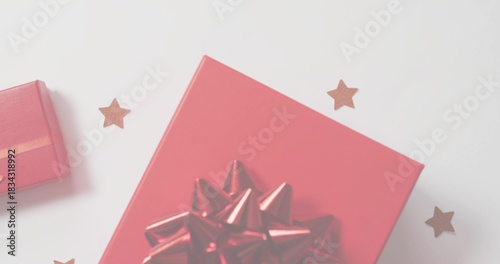 Displaying large red gift box on white table, with shiny bow, small red box, star confetti